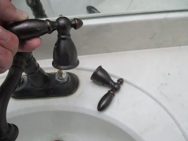 A hand holding a faucet fixture to check how it sits on the sink