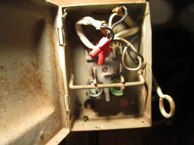 A corroded outdoor electrical disconnect with a red pull handle