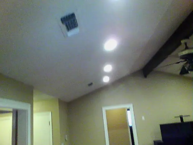 A vaulted ceiling with recessed lights and a vent