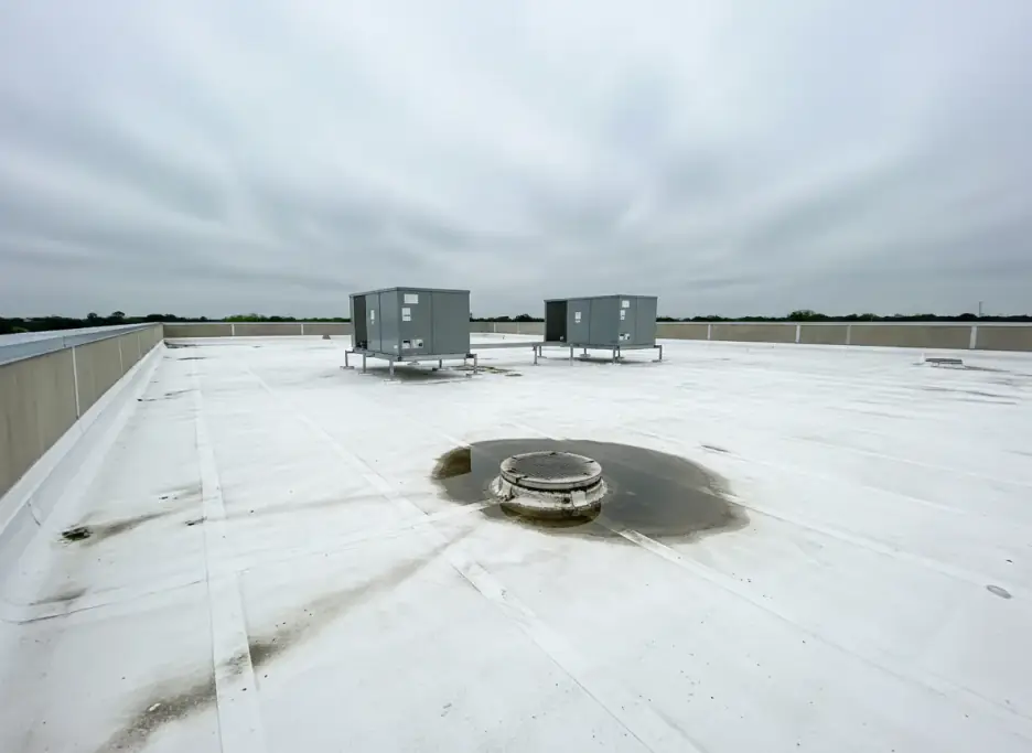 A flat commercial roof with two rooftop HVAC units and standing water at a roof drain, the kind of detail a commercial inspection records