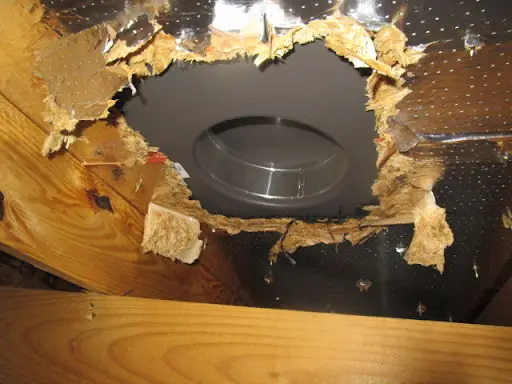 A hole in a ceiling showing a canister light and torn insulation paper above it
