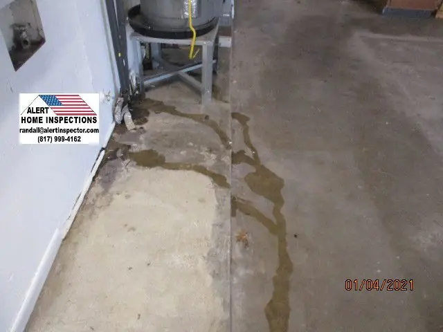 Wet concrete floor beside a water heater, with a small Alert flag-roof sign in the frame